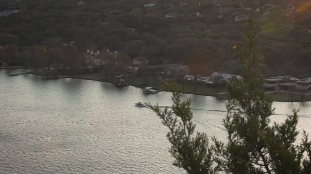 Boat driving on the lake in the distance in slow motion, as seen from above peering through trees