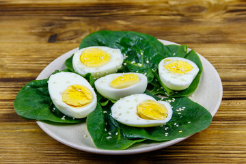 Boiled eggs with fresh spinach leaves and sesame seeds on wooden table