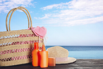 Set of sun protection products and stylish accessories on wooden table near sea