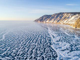 Frozen Lake Baikal, Aerial view. Beautiful winter landscape with clear smooth ice. Famous natural landmark Russia. Blue transparent ice with deep cracks, top view of a frozen lake.