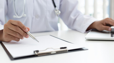 Doctor uses a laptop computer to record patient information and write it on a document to prepare for diagnosis in the room of a modern hospital, Emergency assistance and health care concept.