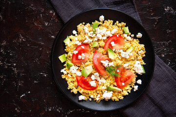 Bulgur porridge with tomatoes, avocado and feta cheese on a dark background