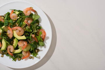 top view of fresh green salad with pumpkin seeds, shrimps and avocado on plate on white background