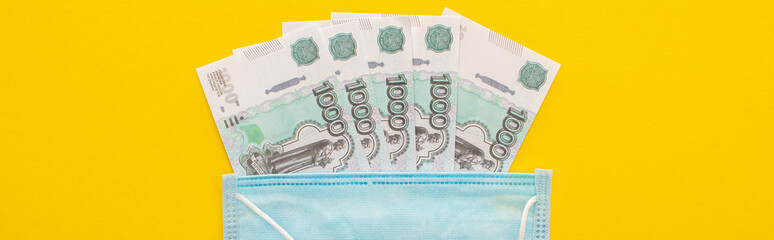 top view of Russian banknotes and medical mask on yellow background, panoramic shot