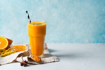 Turmeric smoothie in glass with ingredients, turmeric powder, ginger and spice on blue - obrazy, fototapety, plakaty