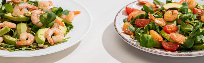 fresh green salad with shrimps and avocado on plates  on white background, horizontal image