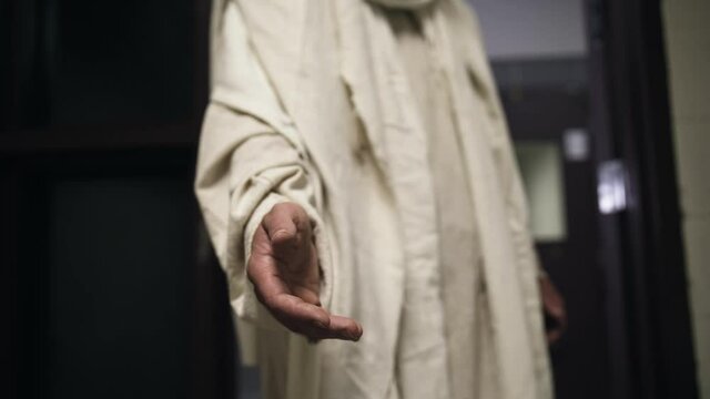 Jesus wearing a white robe extends his hand to a prisoner in his cell