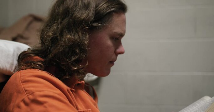 A Man Wearing An Orange Jumpsuit In His Prison Cell Reading A Bible