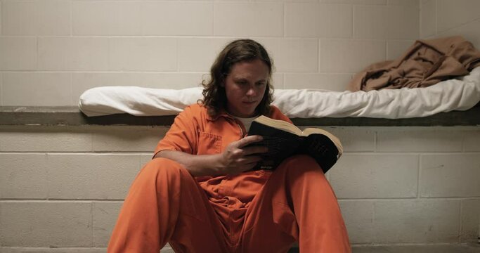 A prisoner sits next to his bed in prison reading a bible