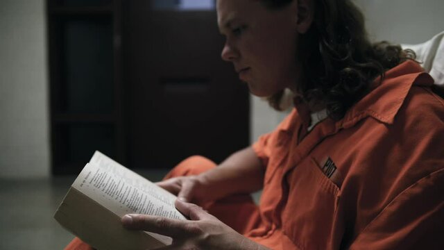 A prisoner reads a bible in his cell while wearing an orange jumpsuit