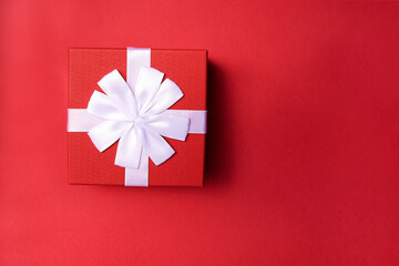 Decorative red gift box with white ribbon on red background. Top view. Space for text