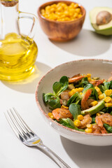top view of fresh green salad with shrimps and avocado on plate near cutlery on white background