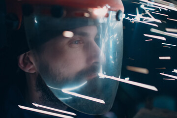 Adult man in transparent protective mask with flying metal sparks to face
