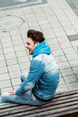 High angle view of cheerful man sitting on bench near walkway