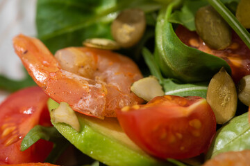 close up view of fresh green salad with pumpkin seeds, cherry tomatoes, shrimps and avocado