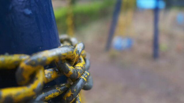Chipped yellow chain links in the foreground with a swaying swing in the background