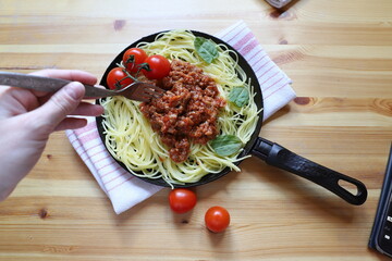 Delicious spaghetti on a fork with a typical Italian sauce to try from the pan, cooking at home, pasta in a pan on a wooden background