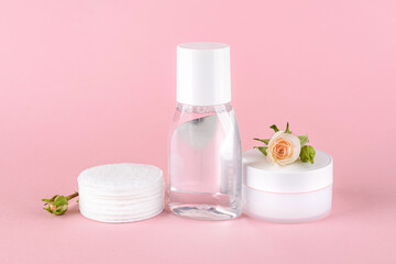 Obraz na płótnie Canvas Skin tonic lotion or micellar water, cotton pads, facial cream and small roses on a pastel pink background. Cosmetics for moisturizing and cleansing. Skin, hair or body care.
