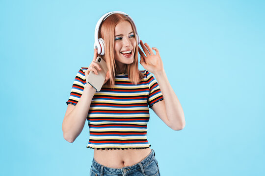 Image of cheerful caucasian girl using wireless headphones and cellphone