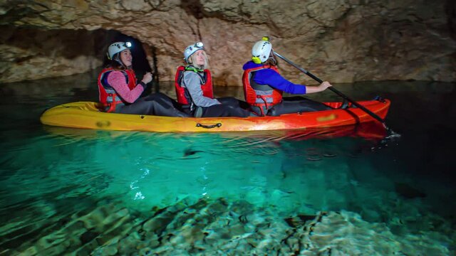 Three women on kayak in underground emerald waters of Peca, Slovenia.