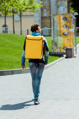 Back view of courier with thermo backpack walking on urban street