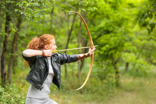 Sporty young woman practicing archery outdoors