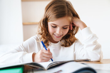 Photo of happy girl writing in exercise book while doing homework