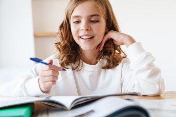 Photo of happy girl writing in exercise book while doing homework