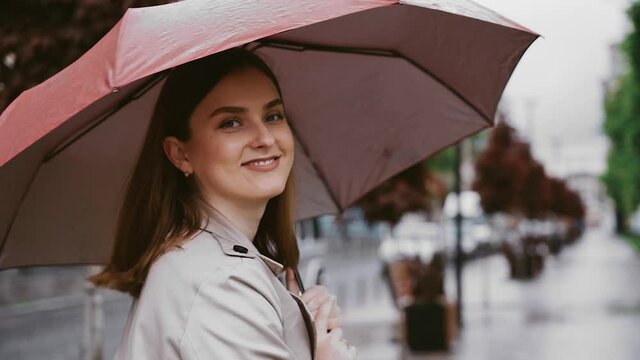 A young, attractive woman with an open umbrella strolls through a rainy the street The girl looks very happy walking in nature. tracking shot. in slow motion.