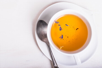 Cup of green tea with flower petals with a spoon on a tea saucer on a white wooden table, top view, copy space