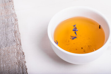 Cup of green tea with flower petals on a white wooden table, top view, close-up