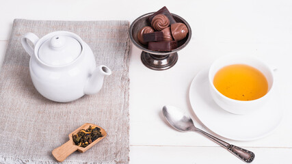 Teapot, cup of green tea with flower petals and candies in a vintage metal vase on a white wooden table