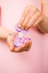 Child's hands with blue and silver color glitter and confetti on pastel pink background.