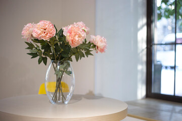 Pink peonies stand in glass vase on table next to the window