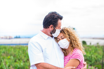 couple of people hugged together and man giving a kiss at his wife - two adults wearing medical and surgical mask on them face to prevent covid-19 or any type of disease or flu - in love concept