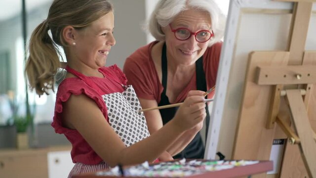 Young girl with grandmother painting on canvas