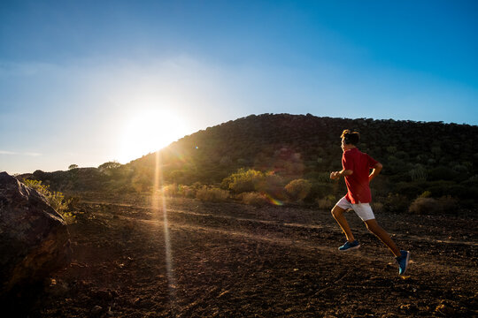 one man teennager running alone and isolated in the mountains or hill listening music to be fitness and healthy - sunset and beautiful sky - jogger lifestyle and concept