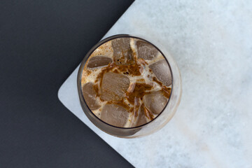 cold coffee summer drink with ice in a glass top view, 
dark wood and white marble background