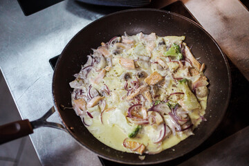Appetizing salmon pieces are fried with mushrooms, broccoli, onion and covered with creamy sauce on the pan on the induction cooker.