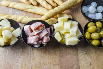 Italian appetizers with green olives, spring onions, porchetta ham, fontina cheese, smoked provola cheese and breadsticks close up