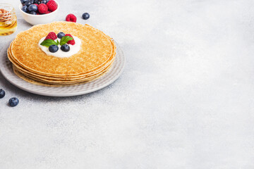 Plate of delicious thin pancakes with berries on grey table Copy space.