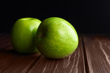 Two green apples over dark wooden background.