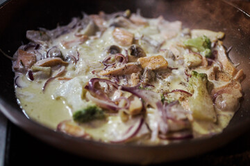 Close up view of salmon fish stewed with onion, broccoli, champignions with creamy sauce on the frying pan. Delicious fish meal cooking process. 