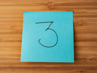 A paper sticker pasted on a wooden surface with the image of the number three