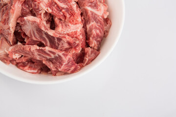 close up copy space shot of sliced raw beef fillet pieces in a white bowl on a white background