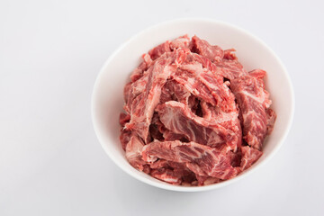 isolated close up top view shot of sliced raw beef fillet pieces in a white bowl on a white background