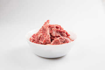 isolated close up side view shot of sliced raw beef fillet pieces in a white bowl on a white background