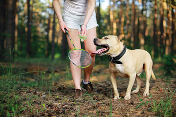 close up view of woman and dog with badminton racket and shuttlecock in forest.