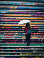 Woman ascending up colourful steps with a white umbrella in the rain.