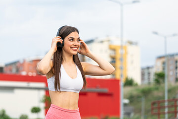 Young woman runner listening to music on earphones. Fit sportswoman taking a break from outdoors training. Woman Listening Music, Doing Workout Exercises On Street.